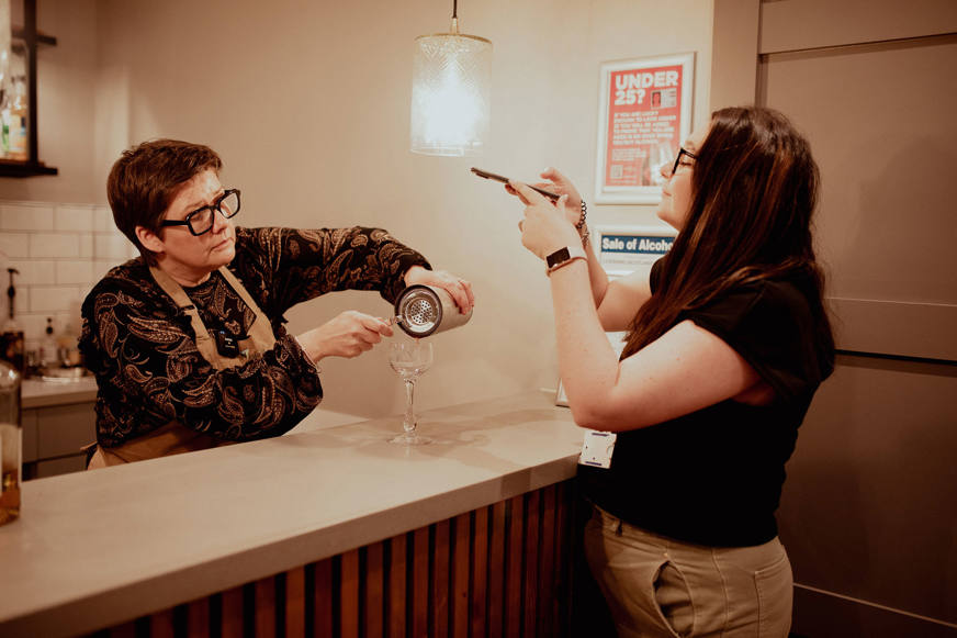woman taking a picture of bartender pouring drink