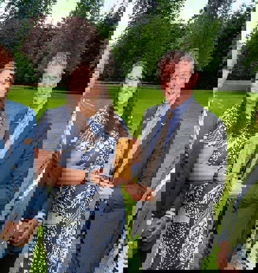 Four people standing on grass holding a wooden award Four people standing on grass holding a wooden award