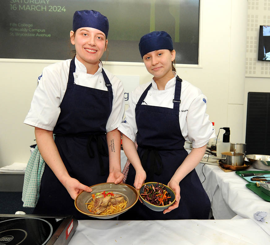 two culinary art students smiling at camera holding their dishes
