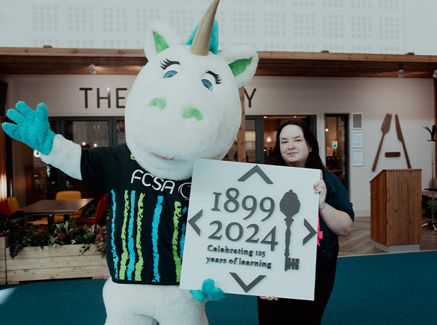 unicorn fcsa mascot and staff member holding 125 sign
