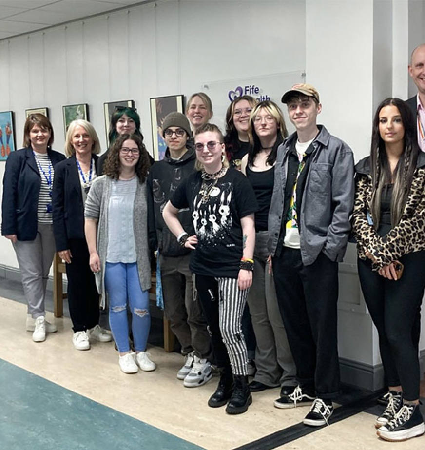A group of people standing in front of a wall of art A group of people standing in front of a wall of art