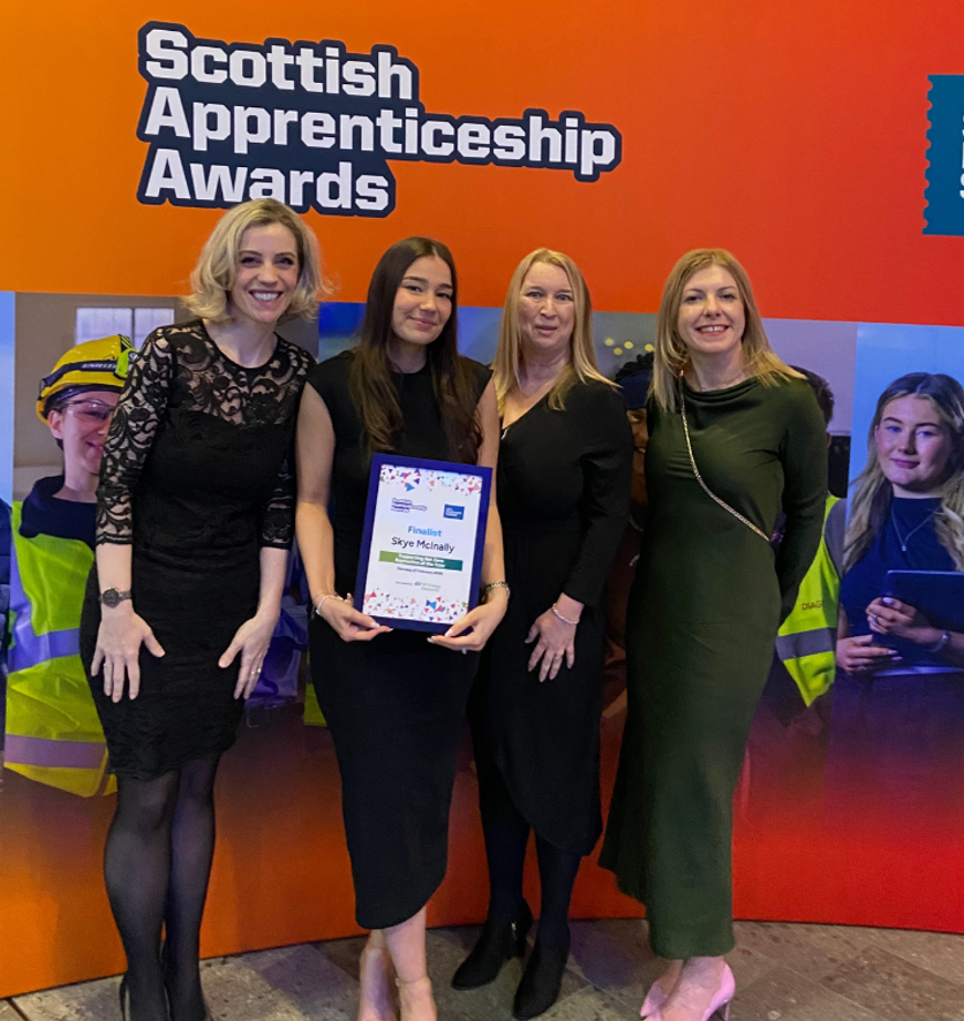 Four women pose at the Scottish Apprenticeship Awards, with finalist holding her certificate in front of the event backdrop.