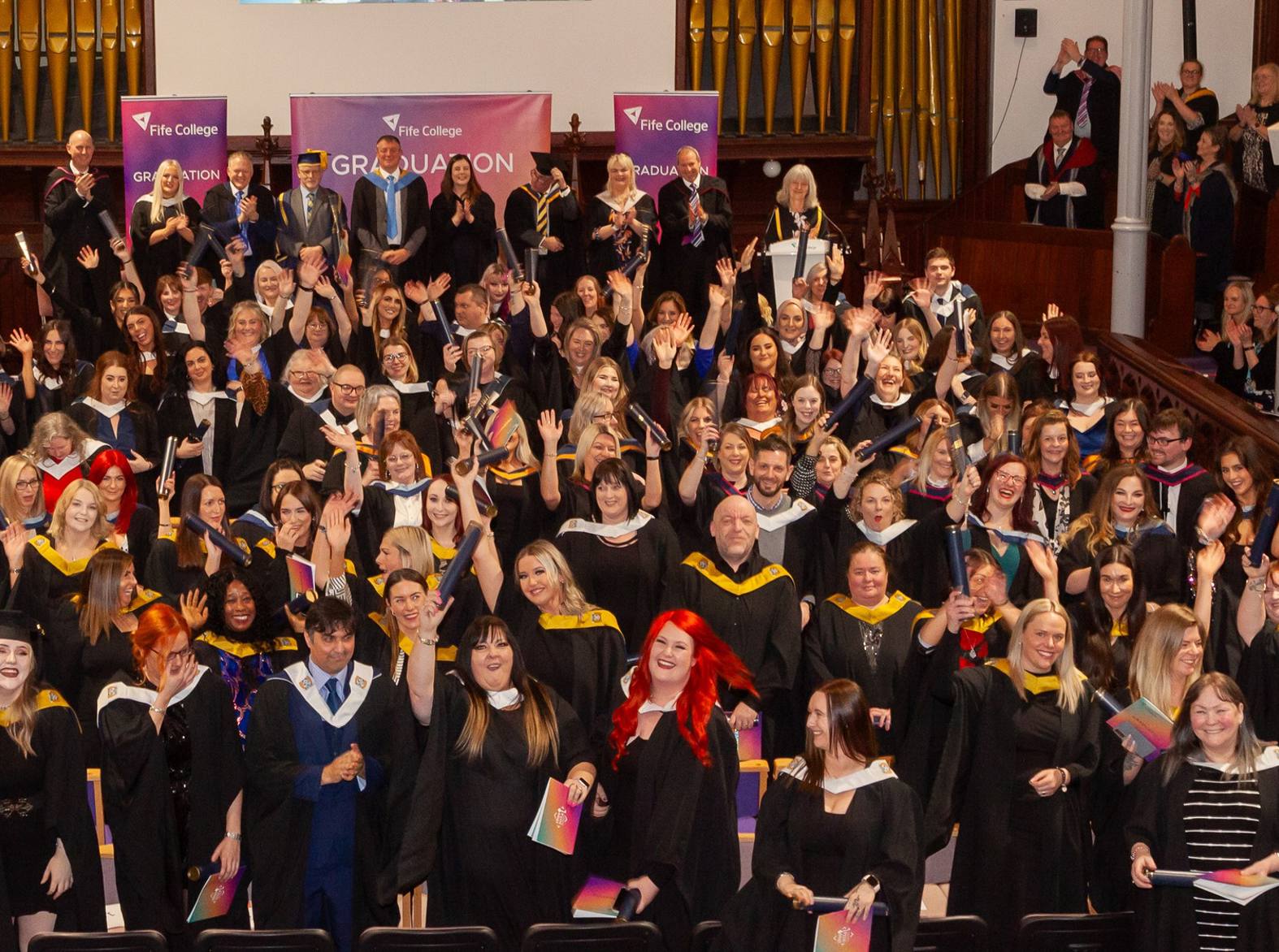 graduates in a crowd smiling at camera holding scrolls