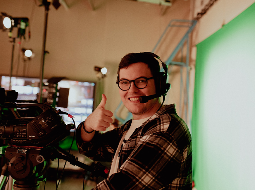 broadcast media student holding thumbs up smiling at camera