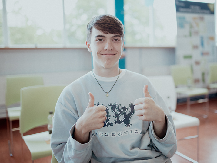 male student smiling at camera with thumbs up