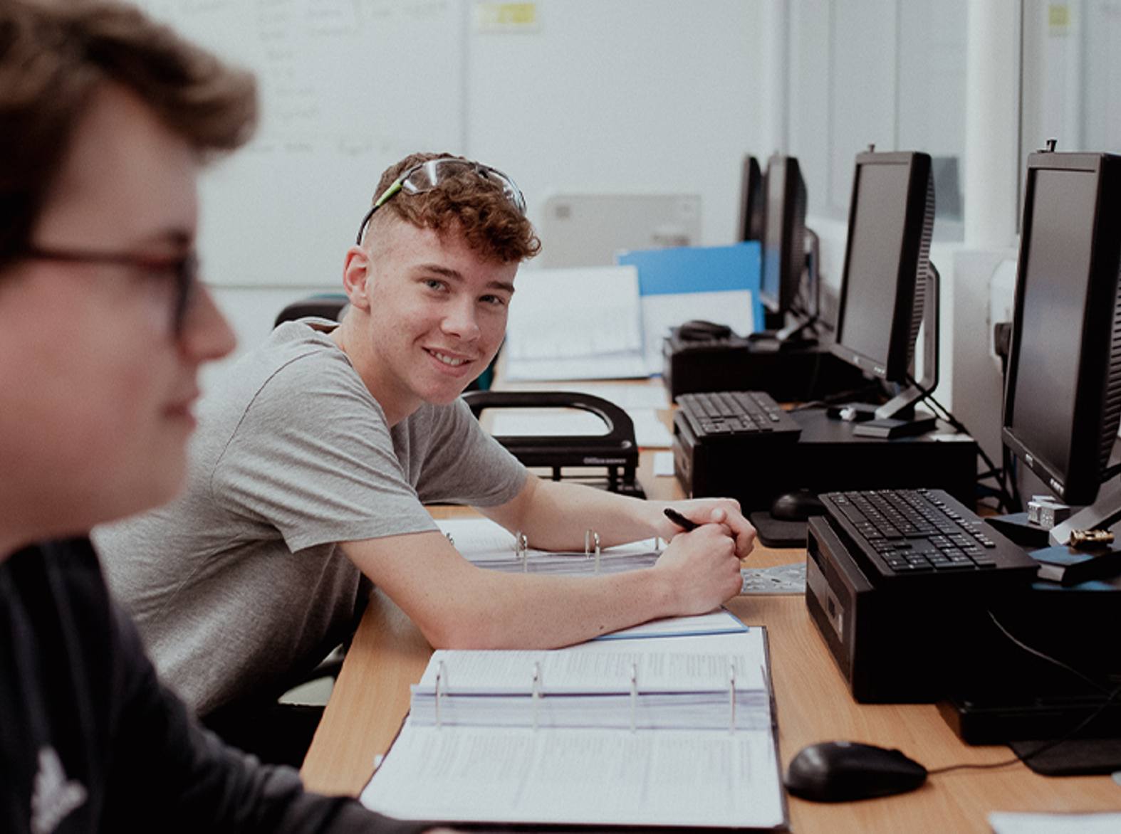 male student sitting in front of computer smiling at camera 