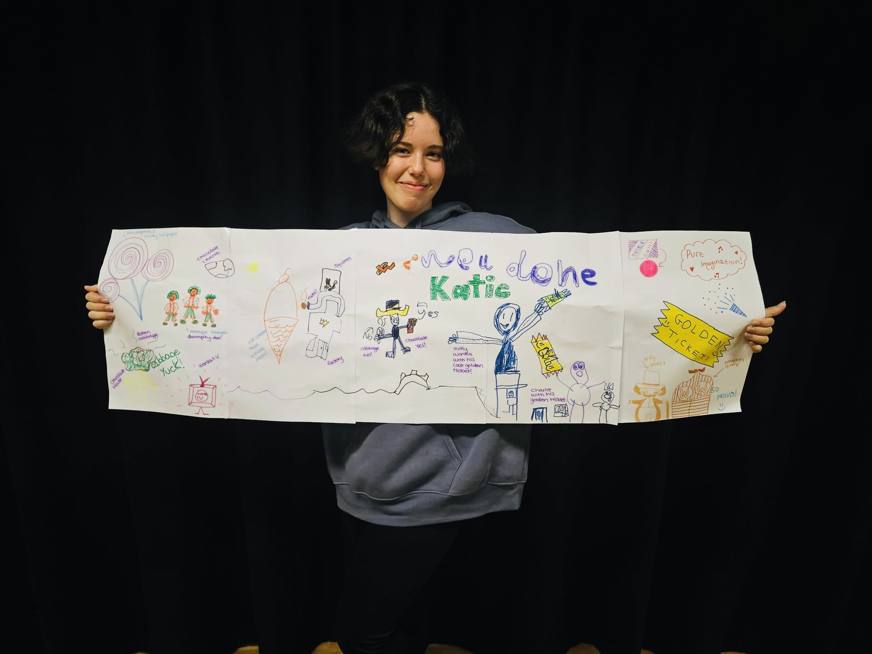 youth theatre student holding banner of drawings up smiling at camera